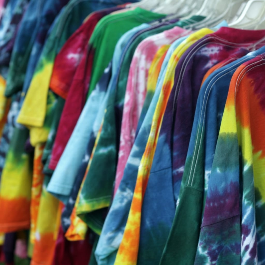 Row of colorful tie-dye T-shirts hanging on a rack, displaying a rainbow of colors including blue, green, yellow, orange, pink, and purple