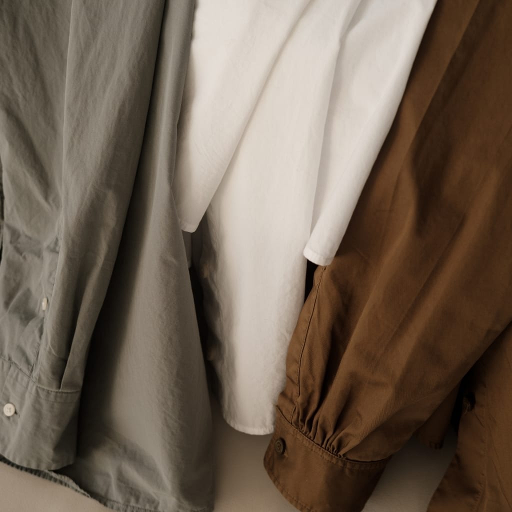 Close-up of three shirts in gray, white, and brown tones hanging side by side.