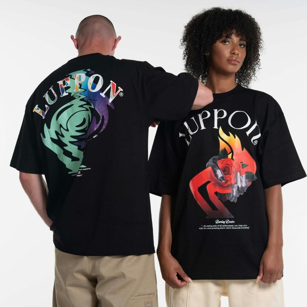 Two models wearing oversized black T-shirts with bold, colorful graphic prints. The man (back view) has a large multicolor design and the word “LUPPON” on his shirt; the woman (front view) wears a shirt with a fiery red and orange graphic and the word “LUPPOLL” across the chest.