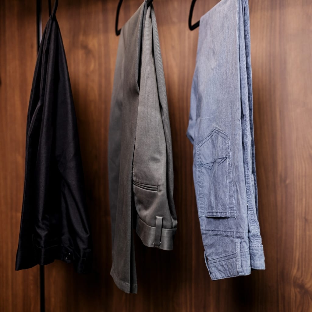 A row of jackets hanging on hooks against a wooden backdrop. From left to right: a dark jacket, a gray coat, and a light blue denim jacket.