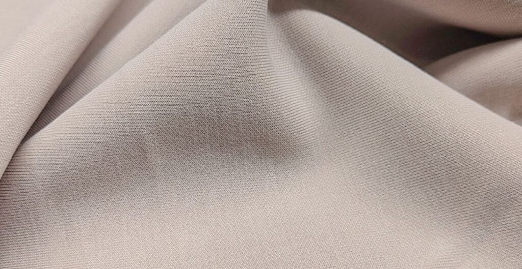 Close-up of smooth beige fabric with fine texture and soft folds.