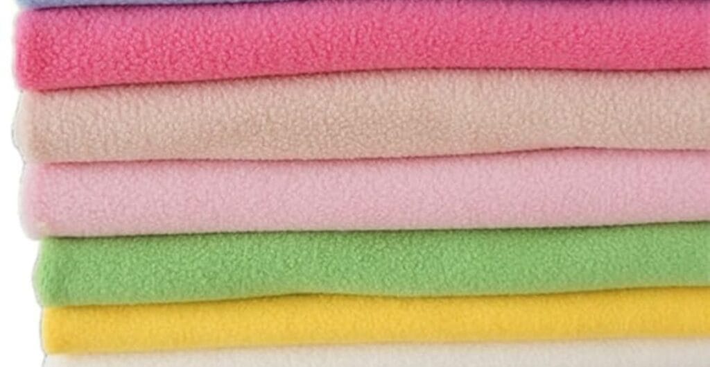 Stack of colorful fleece fabric in pink, beige, green, yellow, and purple shades.