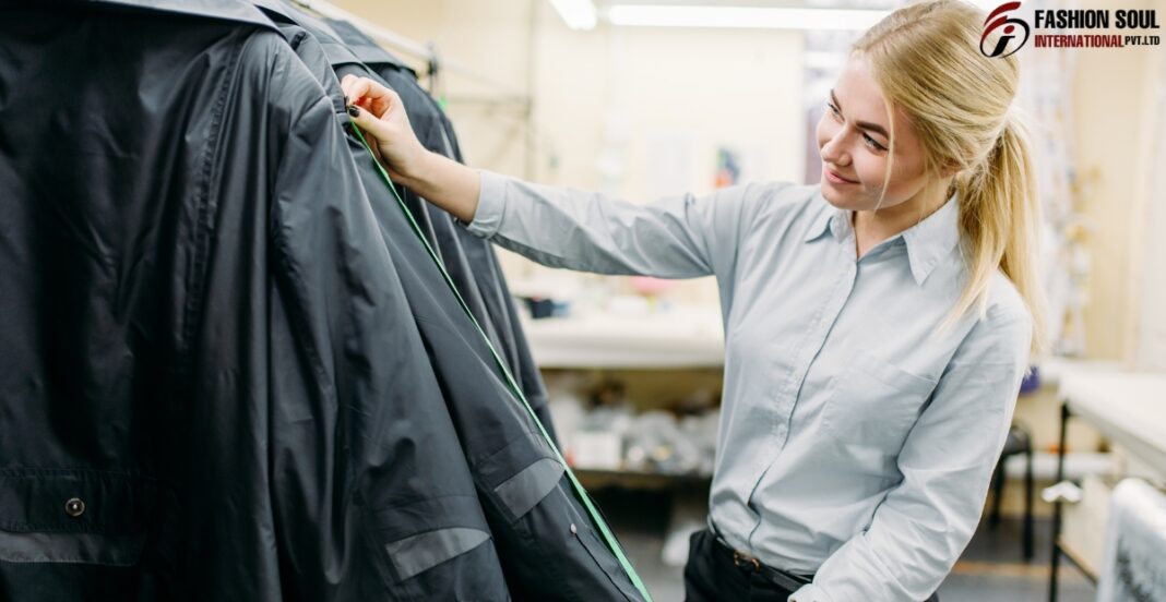 A young woman with blonde hair is smiling and measuring a black jacket on a clothing rack in a retail or tailoring shop.