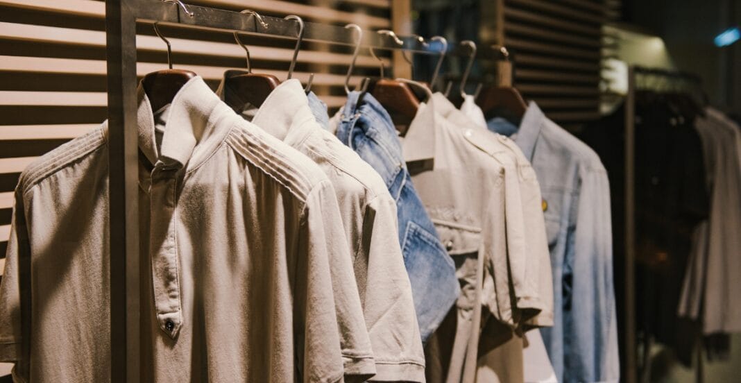 A row of neatly hung shirts on a clothing rack in a shop, featuring neutral colors like beige and light denim, with soft lighting in the background.