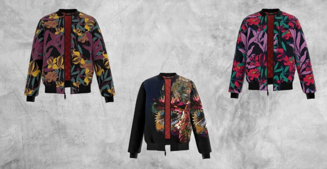 Three colorful bomber jackets with floral and abstract patterns hanging against a plain grey background.