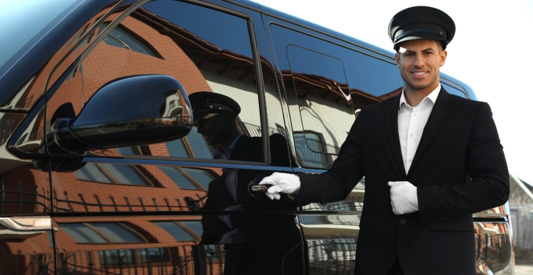 Professional chauffeur in a black suit and white gloves standing beside a luxury black vehicle.
