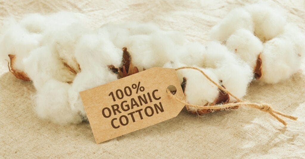 “A close-up of fluffy cotton with a brown tag that reads ‘100% ORGANIC COTTON’ tied with twine.”