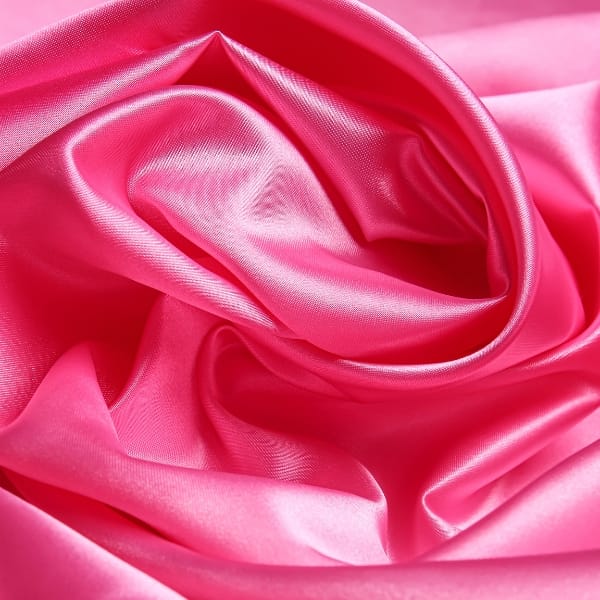 A close-up of bright pink satin fabric, softly folded and twisted into curves with a smooth, glossy sheen.A close-up of bright pink satin fabric, softly folded and twisted into curves with a smooth, glossy sheen.