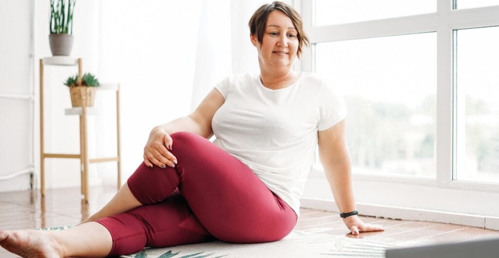 Woman in 3x yoga pants comfortably stretching on a mat