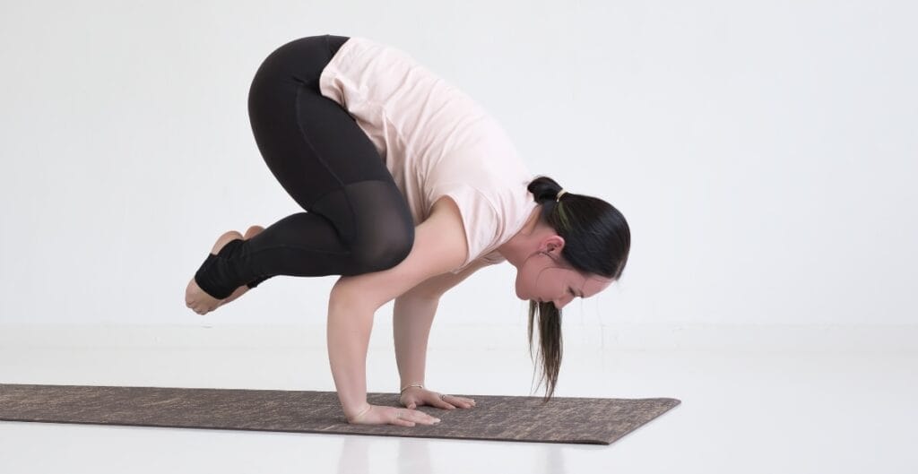 Woman practicing yoga in 4x yoga pants, balancing in a crow pose on a yoga mat