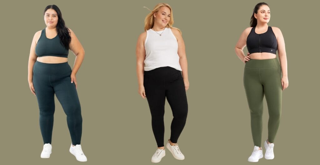 Plus-size woman wearing black leggings, standing with hands on hips and a confident smile against a neutral backdrop.