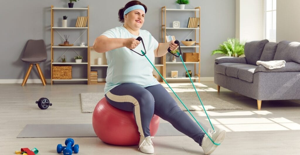 Plus size woman wearing good leggings, using resistance bands for a workout on an exercise ball
