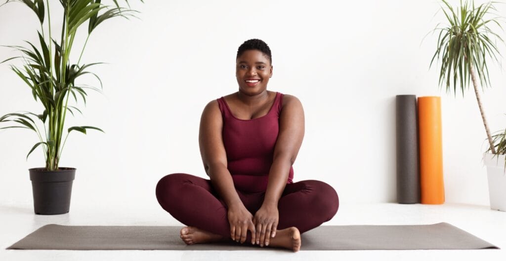 Plus size woman in trendy activewear practices yoga at home, highlighting fashionable exercise outfits designed for comfort and movement.