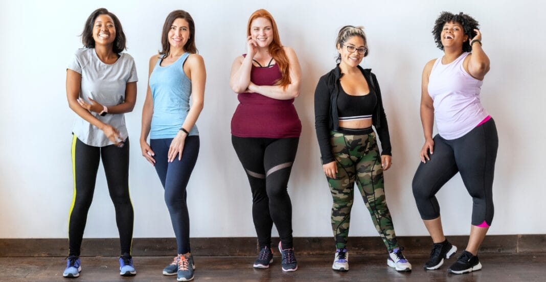 A confident plus-size woman wearing sleek black leggings, standing with hands on hips against a neutral backdrop.