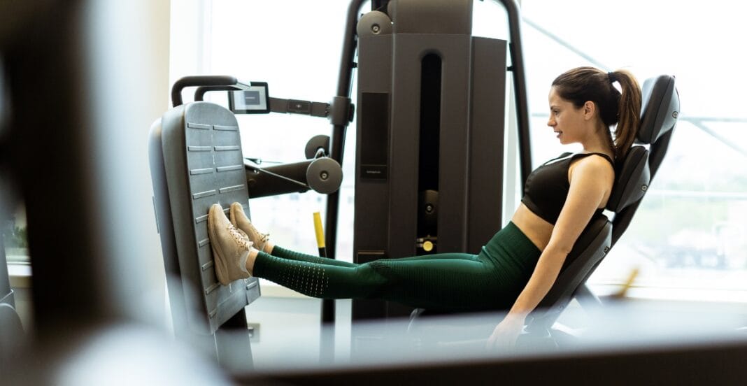 Woman wearing green gym leggings doing a leg press workout at the gym