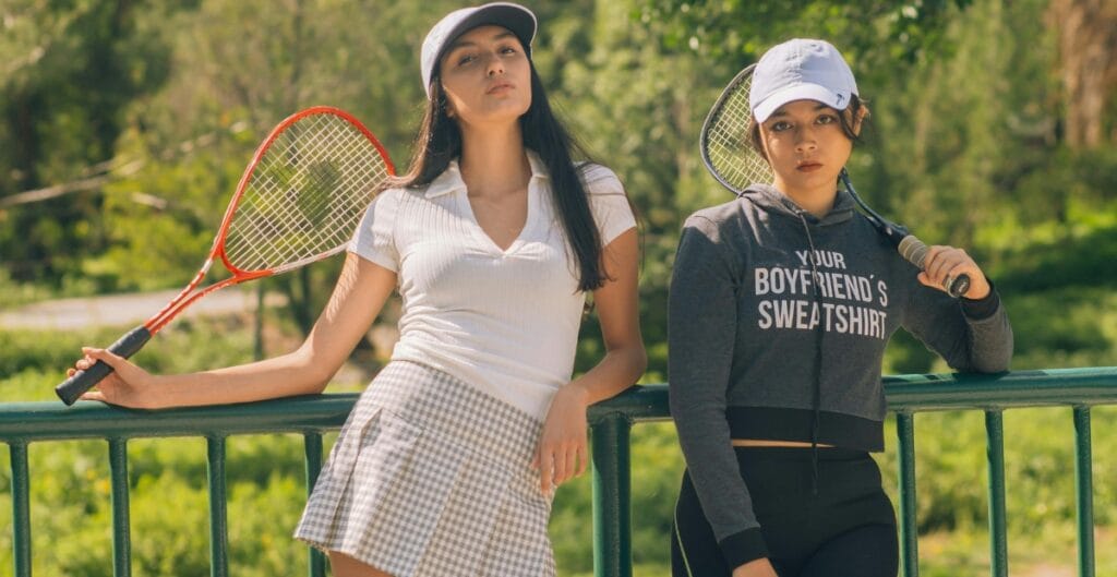 Two women wearing tennis skirts, one in a sweatshirt and the other in a polo, ready for a casual day out