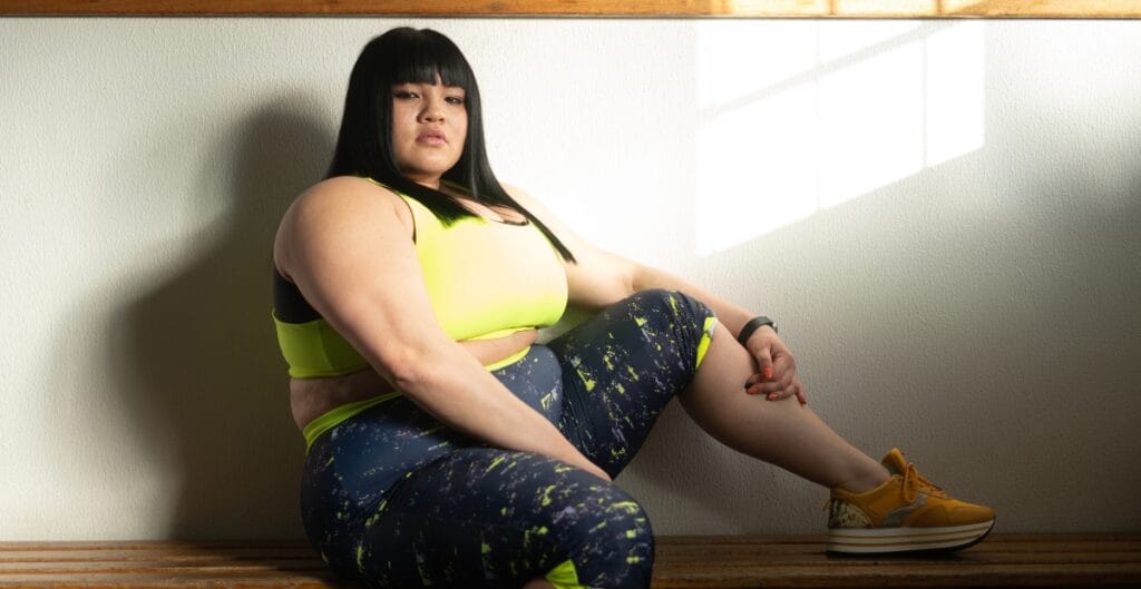 Confident woman in neon yellow activewear posing indoors, showcasing stylish ladies plus size sweat suits.