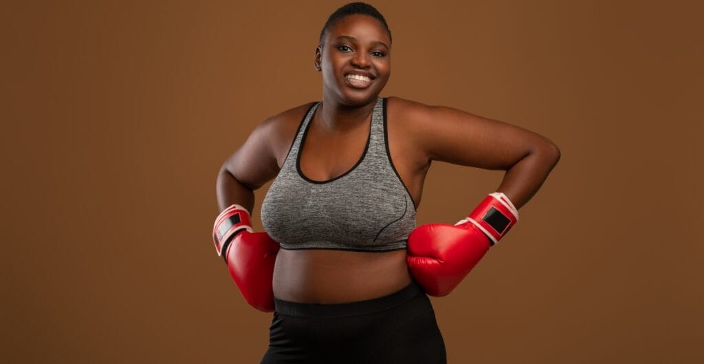 Smiling woman in athletic gear with red boxing gloves, standing strong and proud, highlighting comfort and support with plus size boxers