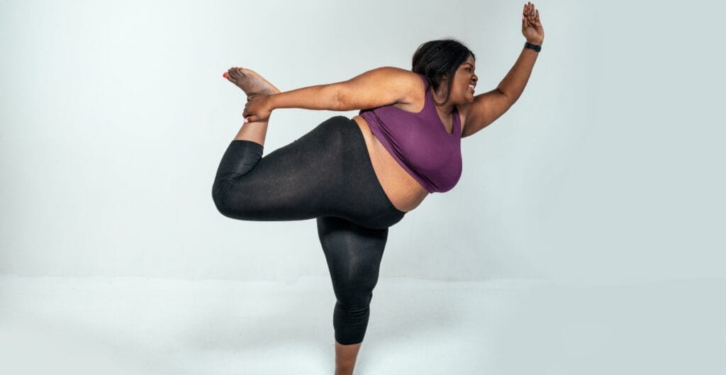 Plus-size woman wearing a purple fitness tank and black leggings performing a yoga pose, showcasing stylish and comfortable activewear for curvy individuals