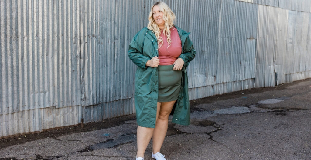 Plus size woman wearing a green skort, pink top, and white sneakers, posing confidently against a metal wall