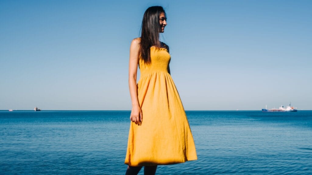 Woman in a yellow Aline midi dress standing by the beach, with a scenic ocean view