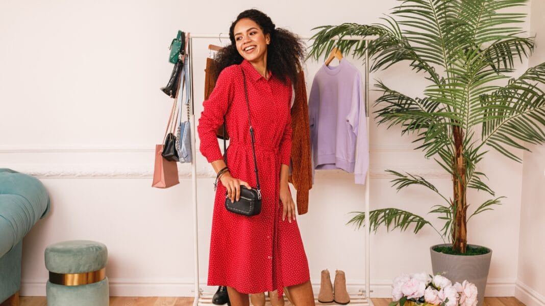 Woman in a red Aline midi dress, styled with a black purse, posing with a clothing rack