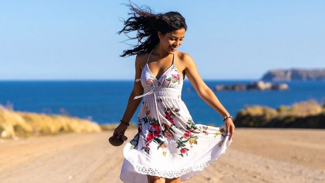 Woman in a floral beach midi dress twirling by the ocean.