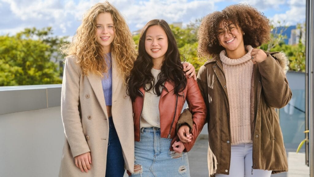 Three curvy tweens standing outdoors, wearing stylish jackets and jeans, looking fashionable and confident.
