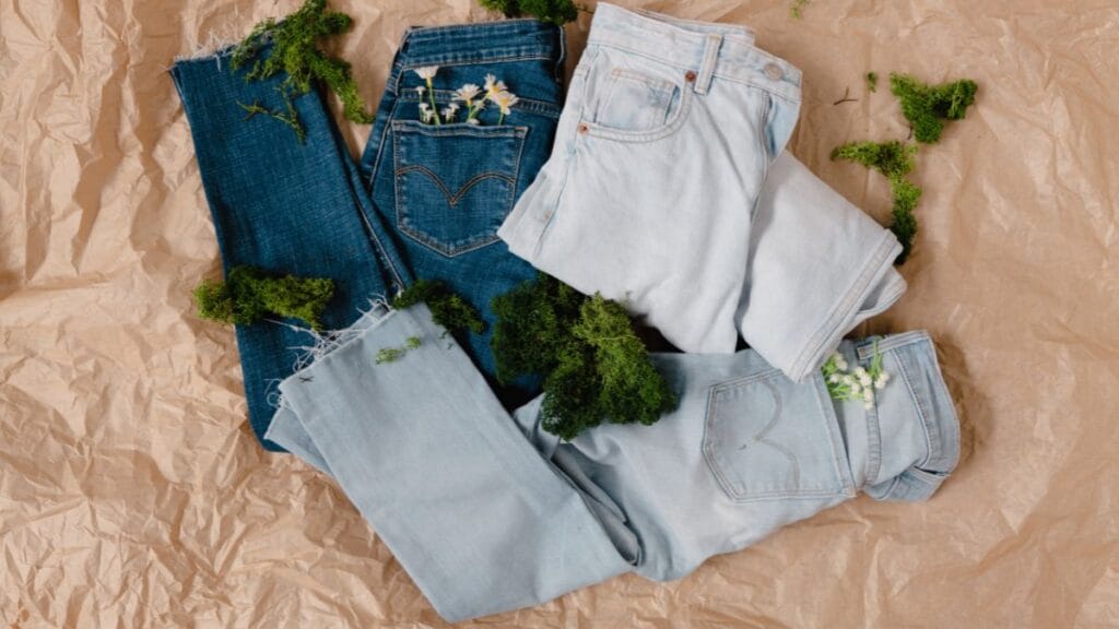 Two pairs of jeans, one dark blue and one light blue, surrounded by greenery on crumpled brown paper