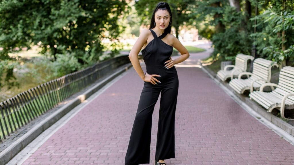 Woman in a black evening jumpsuit with a modern design, striking a pose outdoors.