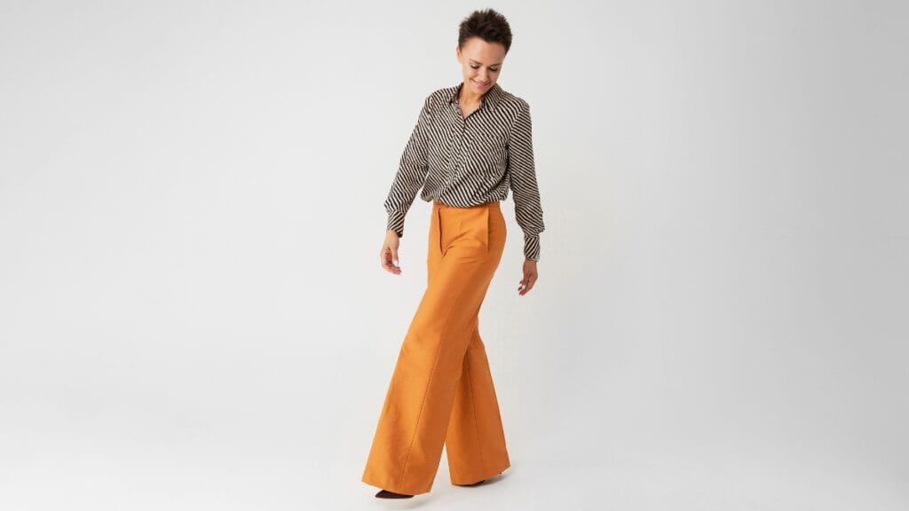 Woman in striped blouse and orange evening pants, walking confidently.