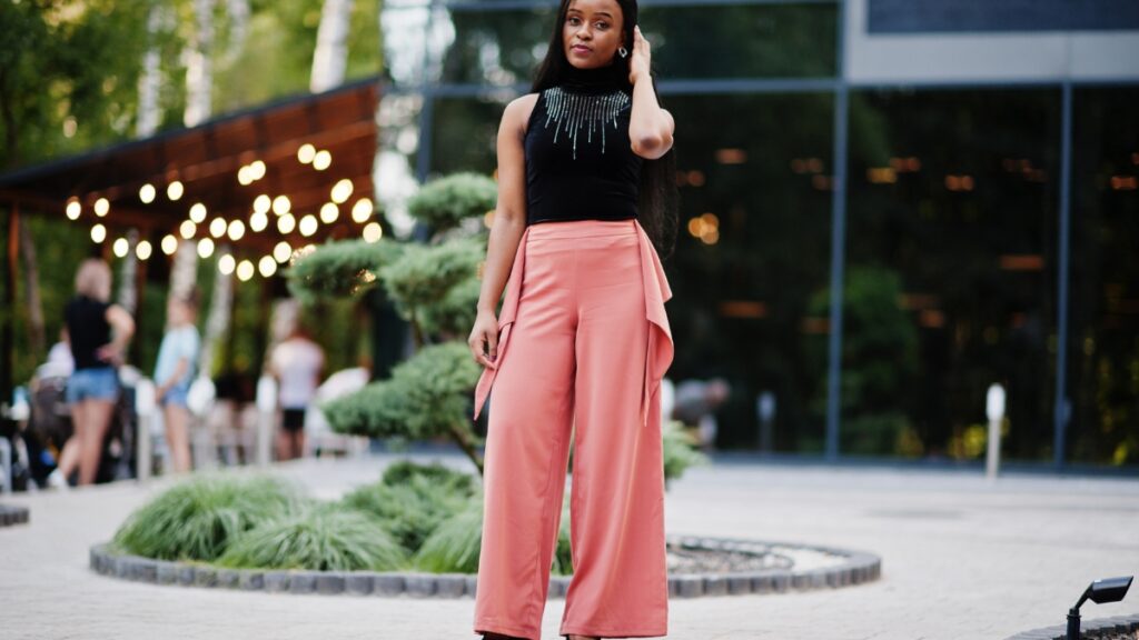 Woman wearing a black top and pink evening pants, standing in a garden setting.