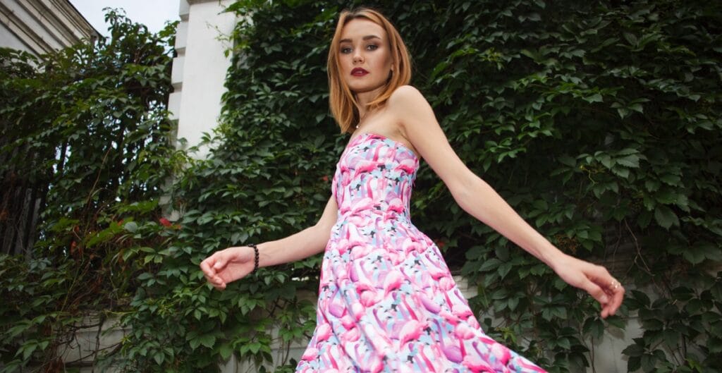 A woman in a vibrant flamingo print midi dress, walking outdoors with confidence.