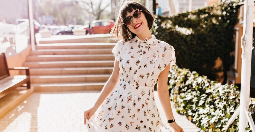 A woman wearing a stylish floral midi dress with sunglasses, posing outdoors.