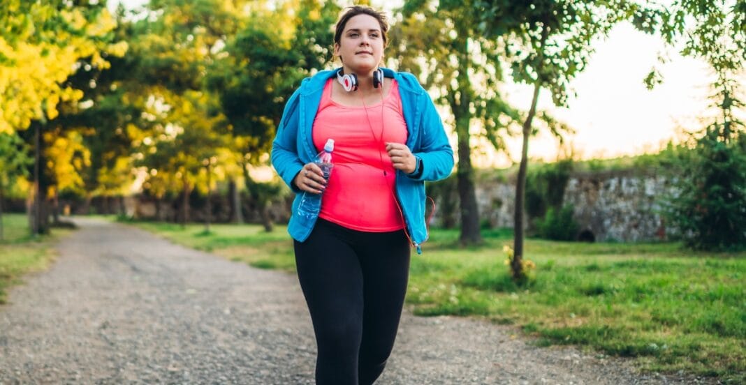 Plus size woman running outdoors in a pink and blue jogger suit, staying active and confident.
