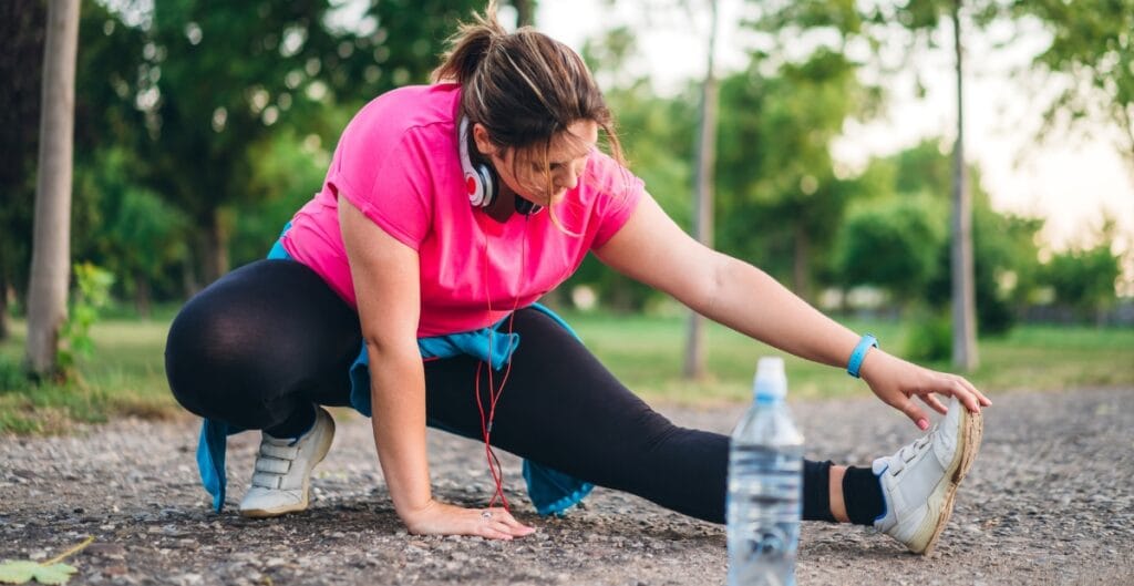 Plus size woman stretching outdoors wearing a pink and black jogger suit for fitness and exercise.