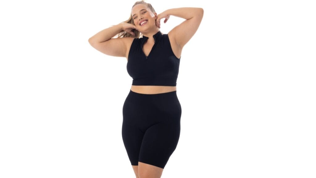 Plus size woman in a black walking shorts set, smiling and stretching with her arms raised
