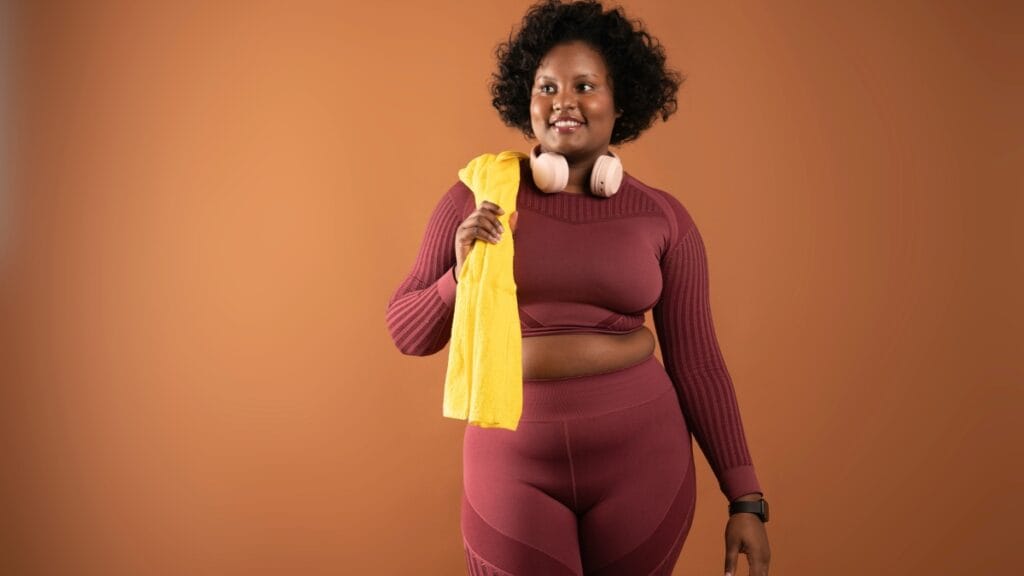 Plus size woman wearing maroon activewear and a yellow towel, ready for a workout session
