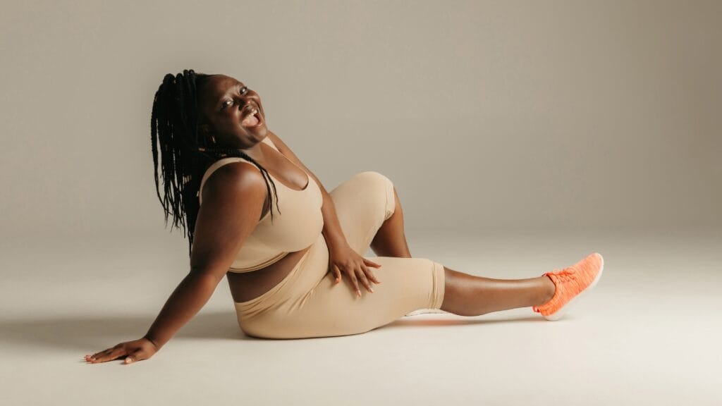 Plus-size woman joyfully wearing a tan outfit, showing confidence and happiness