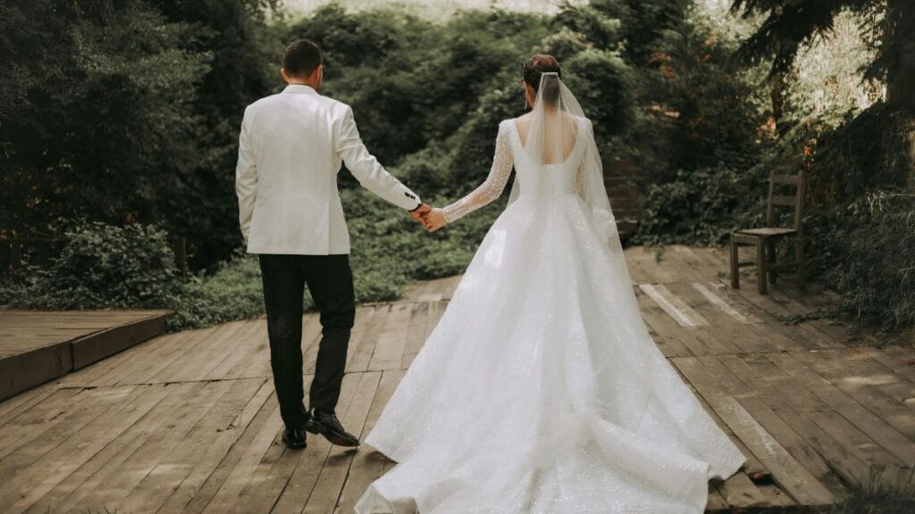 Bride and groom holding hands in a forest, with the bride in a flowing white wedding dress