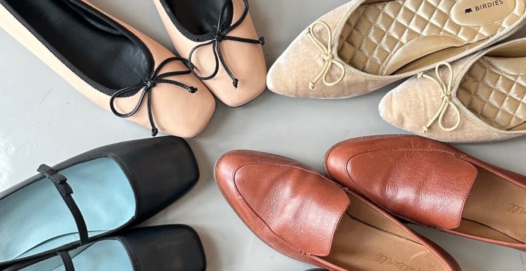 "A stylish pair of insulated winter flats in patent leather, photographed on a snowy sidewalk with a fashionable coat in the background."