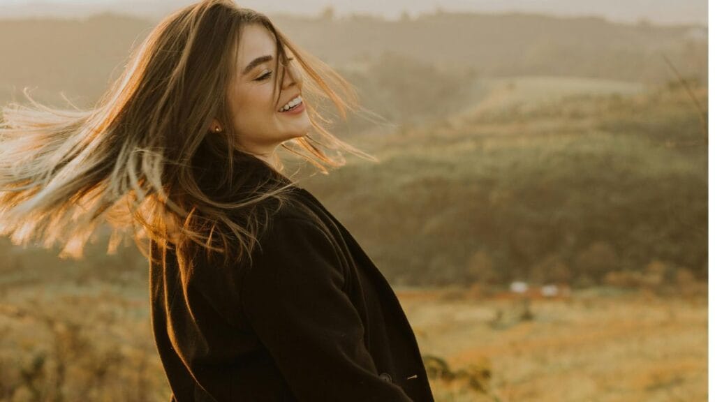“Woman smiling outdoors while wearing a warm fleece lined long coat during golden hour.”