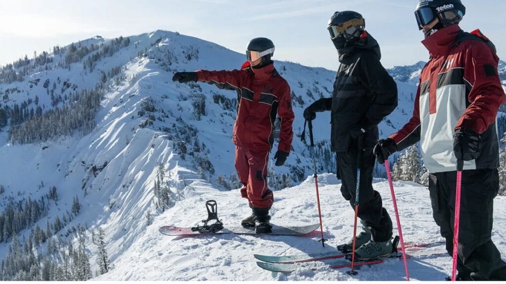 "Three skiers standing together in snowy mountains, wearing colorful mens ski jackets and preparing for their descent."