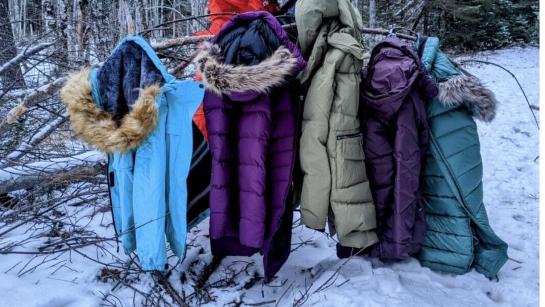 A collection of colorful womens hooded winter coats hanging on a clothesline in a snowy forest.