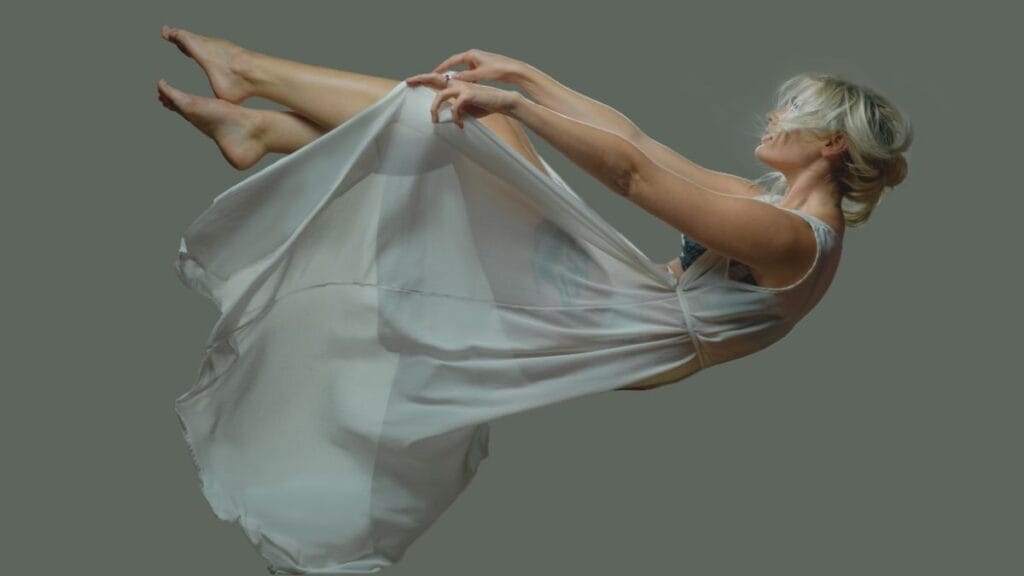 A woman floating mid-air in a flowing white dress, her bare feet off the ground, with a dreamy expression.