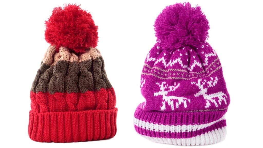 Two colorful knitted winter hats with pom-poms, one red and the other purple, featuring festive patterns and thick ribbed cuffs.