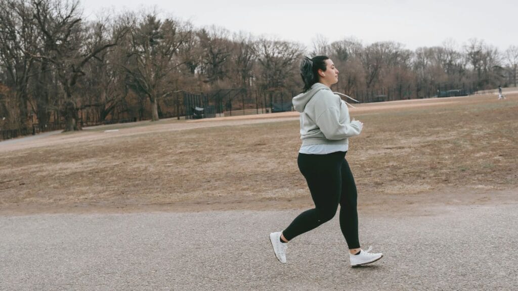 Woman jogging outdoors in black workout pants and a hoodie on a cloudy day.