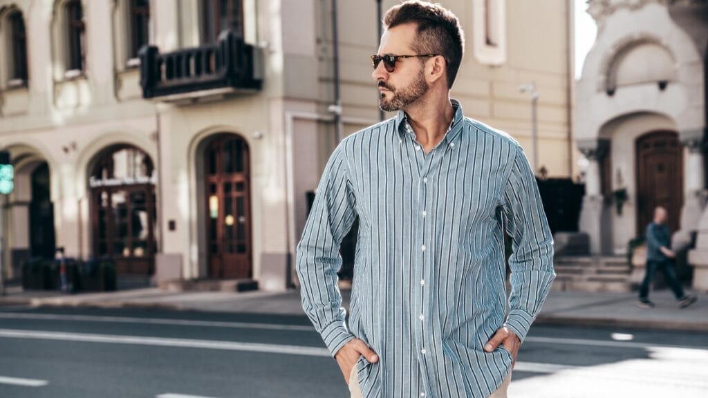 A man wearing a striped big men's casual shirt, walking on the street with a confident look
