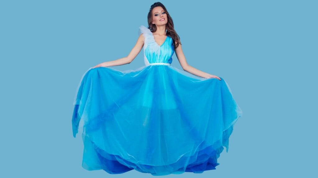 Woman in a blue tulle gown with feather details, standing against a blue backdrop