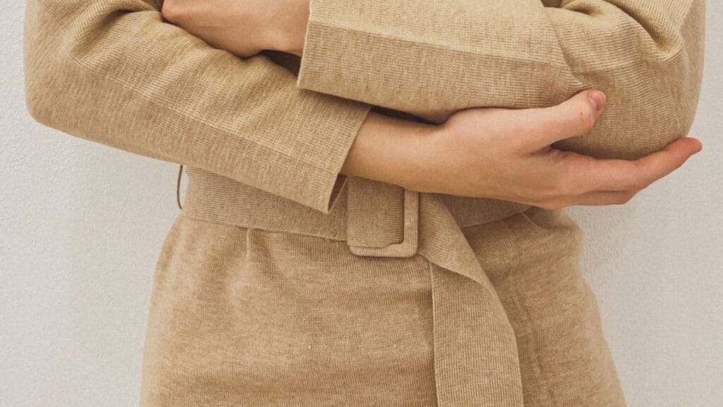 Close-up of a person wearing a beige dress with a belt, showing the sleeves and waist area.